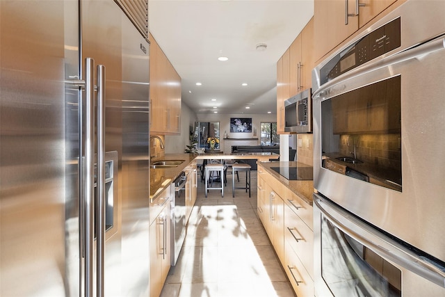 kitchen featuring light tile patterned flooring, appliances with stainless steel finishes, light brown cabinetry, sink, and kitchen peninsula