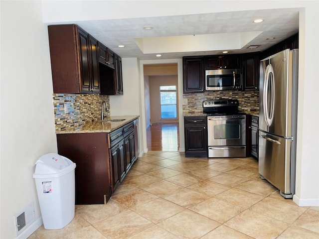 kitchen with light stone countertops, appliances with stainless steel finishes, sink, and dark brown cabinets