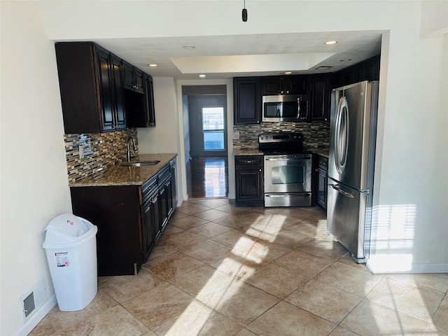 kitchen with sink, appliances with stainless steel finishes, backsplash, stone countertops, and a raised ceiling