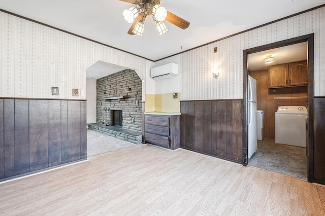 unfurnished living room with crown molding, light hardwood / wood-style flooring, a wall mounted AC, a fireplace, and washer / dryer