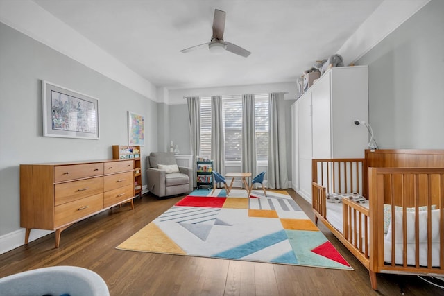 bedroom featuring ceiling fan, a crib, and dark hardwood / wood-style floors