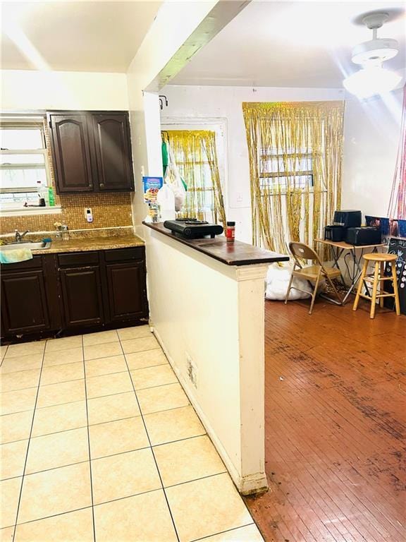 kitchen with sink, dark brown cabinets, decorative backsplash, kitchen peninsula, and light wood-type flooring