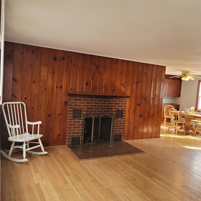 living room with a fireplace, ceiling fan, wood walls, and light hardwood / wood-style floors