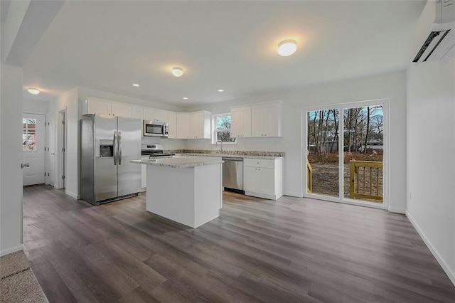 kitchen with appliances with stainless steel finishes, white cabinetry, a center island, a wall mounted air conditioner, and wood-type flooring