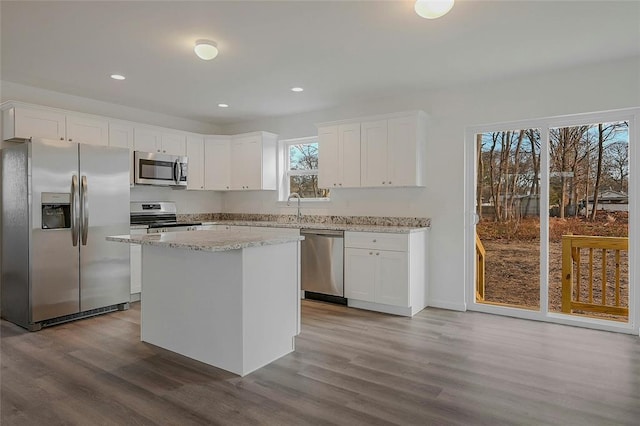 kitchen featuring light stone counters, a center island, light wood-type flooring, appliances with stainless steel finishes, and white cabinets