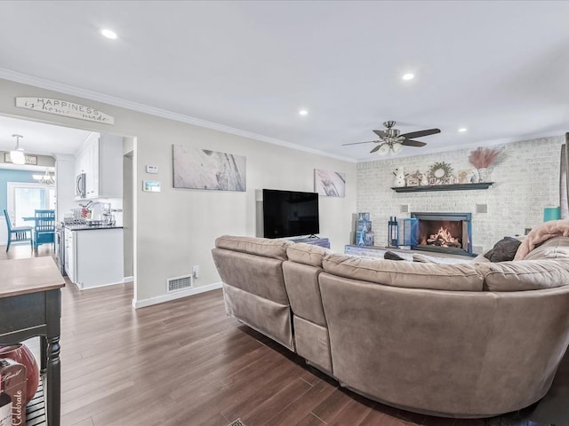 living room with ornamental molding, a fireplace, dark hardwood / wood-style flooring, and ceiling fan with notable chandelier