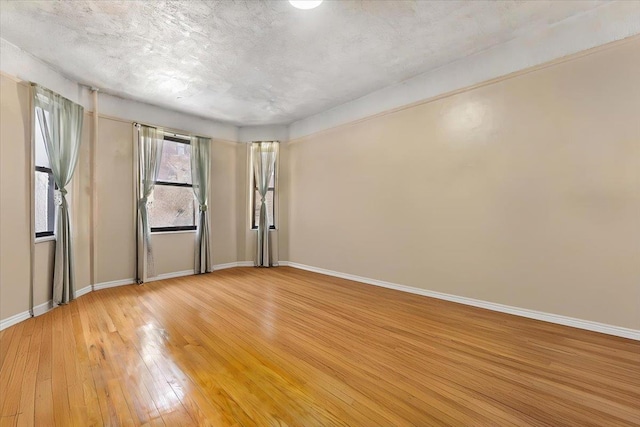 unfurnished room with a textured ceiling and light wood-type flooring