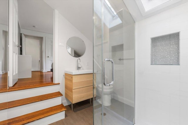 full bathroom featuring toilet, a stall shower, wood finished floors, a skylight, and vanity