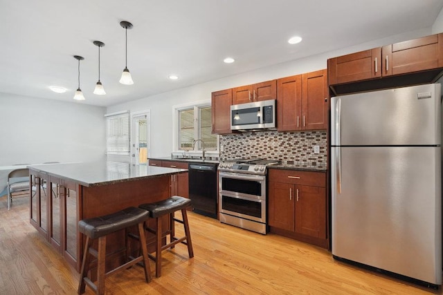 kitchen with light hardwood / wood-style flooring, a breakfast bar area, stainless steel appliances, a kitchen island, and decorative light fixtures