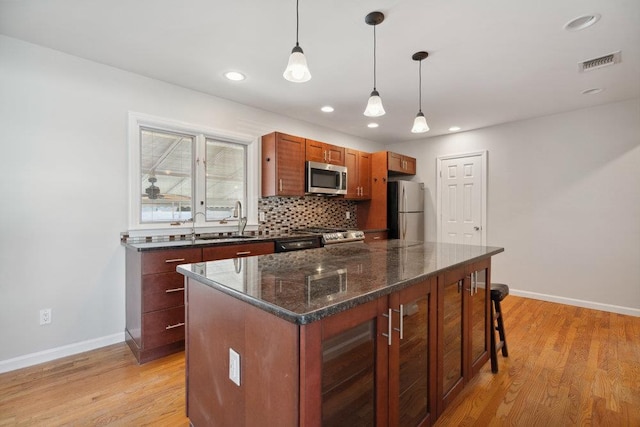 kitchen with a kitchen island, appliances with stainless steel finishes, decorative light fixtures, backsplash, and light wood-type flooring