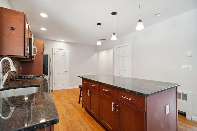 kitchen featuring sink, tasteful backsplash, decorative light fixtures, radiator heating unit, and a kitchen island