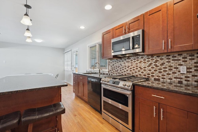 kitchen with sink, decorative light fixtures, light wood-type flooring, appliances with stainless steel finishes, and backsplash