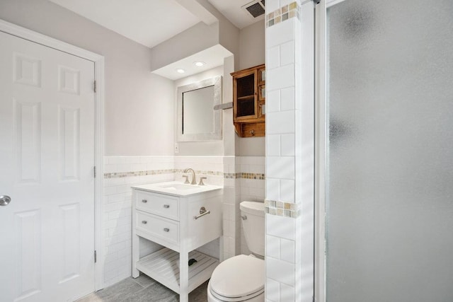 bathroom with vanity, toilet, tile walls, and a shower