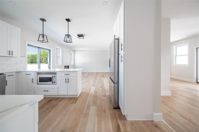 kitchen featuring hanging light fixtures, light wood-type flooring, white cabinets, and appliances with stainless steel finishes