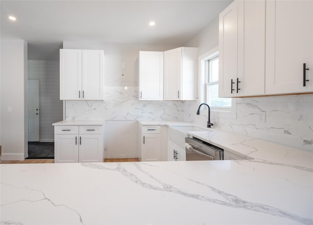 kitchen featuring light stone counters, dishwasher, sink, and white cabinets