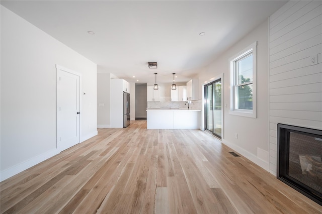 unfurnished living room featuring a fireplace, sink, and light hardwood / wood-style flooring