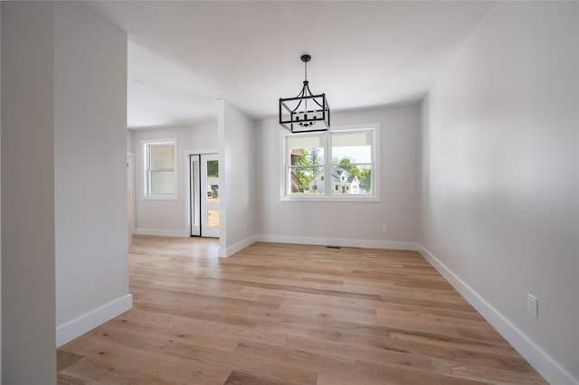 unfurnished dining area featuring an inviting chandelier and light hardwood / wood-style floors