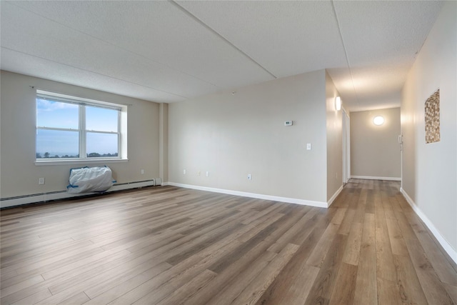 empty room featuring a baseboard heating unit and hardwood / wood-style flooring