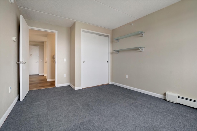 unfurnished bedroom with dark colored carpet, baseboard heating, and a closet