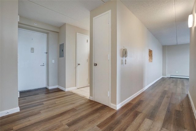 hall featuring hardwood / wood-style floors, electric panel, a textured ceiling, and baseboard heating