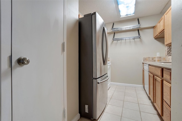 kitchen featuring light tile patterned floors, stainless steel fridge, dishwasher, a textured ceiling, and light brown cabinetry