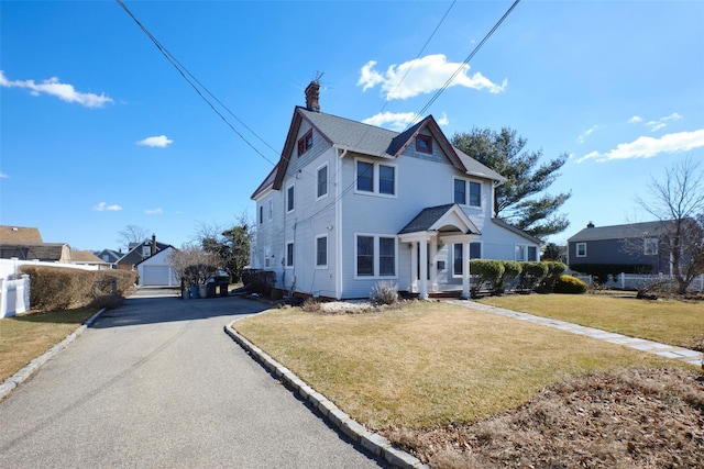 view of front facade featuring aphalt driveway, an outbuilding, a chimney, fence, and a front lawn