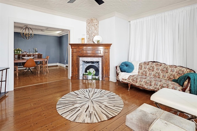 living area featuring ceiling fan with notable chandelier, hardwood / wood-style floors, a high end fireplace, and baseboards