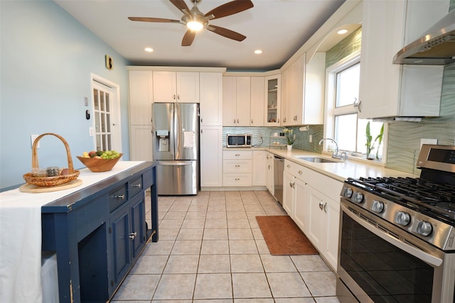 kitchen with stainless steel appliances, a sink, white cabinetry, blue cabinetry, and wall chimney exhaust hood