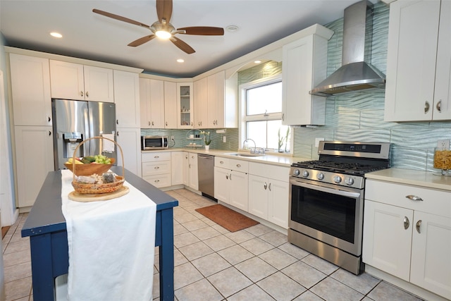 kitchen featuring light tile patterned floors, decorative backsplash, wall chimney exhaust hood, stainless steel appliances, and a sink