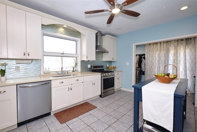 kitchen featuring light tile patterned floors, appliances with stainless steel finishes, white cabinetry, a sink, and wall chimney exhaust hood