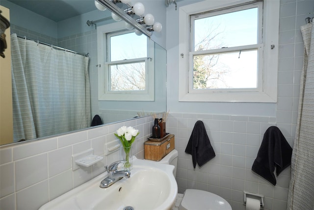 full bath with curtained shower, a sink, toilet, and tile walls