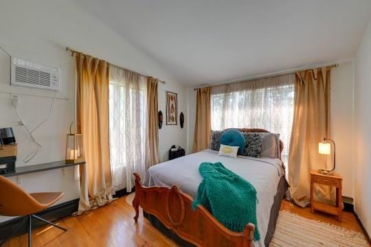 bedroom featuring lofted ceiling, multiple windows, a wall unit AC, and wood finished floors