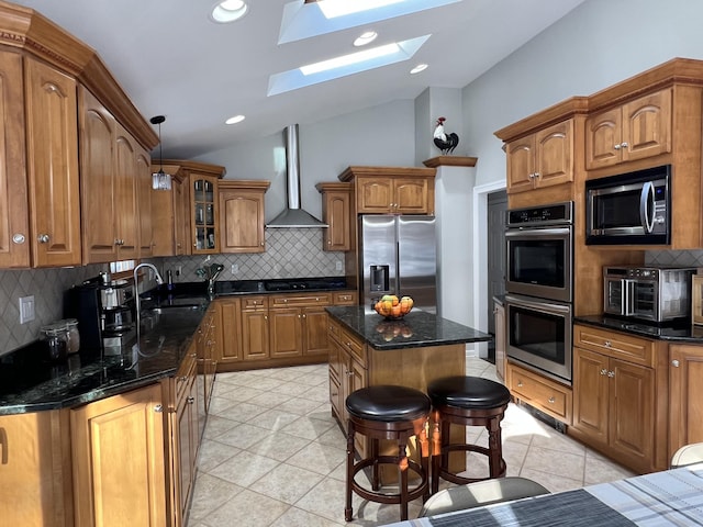 kitchen featuring vaulted ceiling with skylight, sink, a center island, stainless steel appliances, and wall chimney exhaust hood