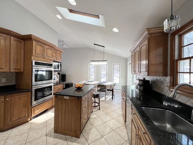 kitchen with appliances with stainless steel finishes, vaulted ceiling with skylight, decorative light fixtures, sink, and a center island