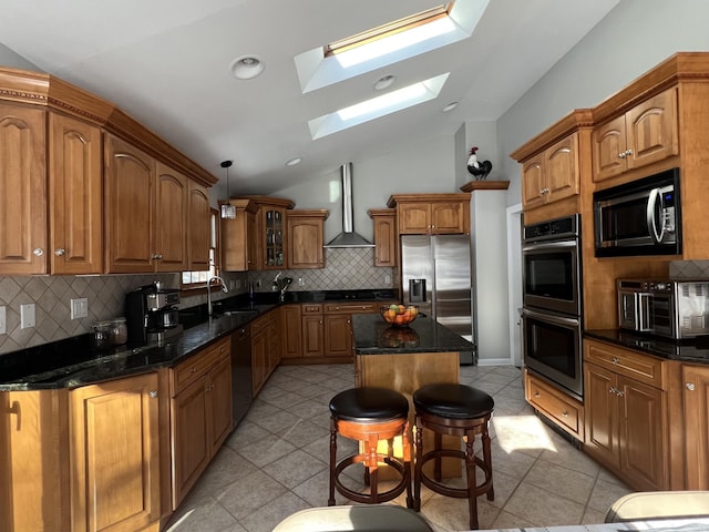 kitchen featuring a breakfast bar, vaulted ceiling with skylight, a center island, stainless steel appliances, and wall chimney exhaust hood