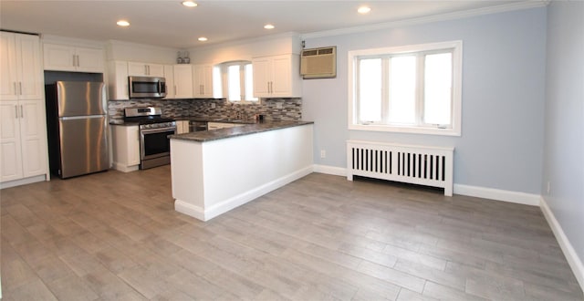 kitchen featuring white cabinetry, tasteful backsplash, radiator, kitchen peninsula, and stainless steel appliances