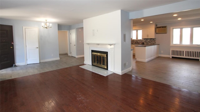 unfurnished living room featuring an inviting chandelier, radiator, dark wood-type flooring, and a wall mounted AC