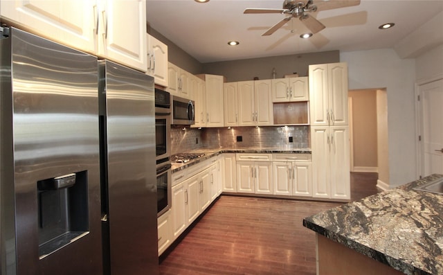 kitchen with dark wood-type flooring, dark stone countertops, stainless steel appliances, white cabinets, and decorative backsplash