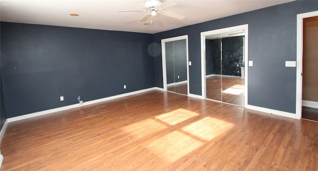 unfurnished bedroom with ceiling fan, wood-type flooring, and multiple closets