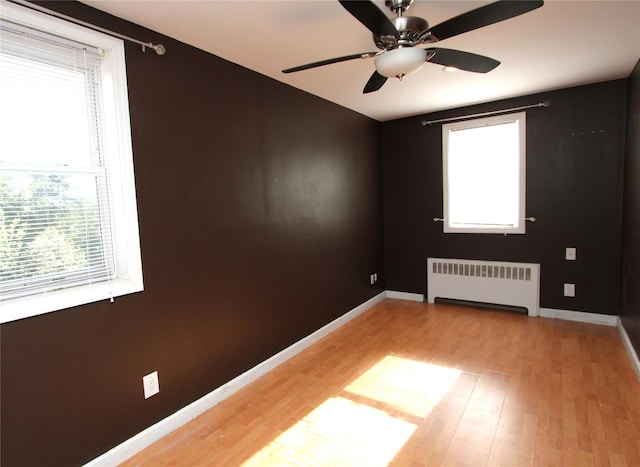 spare room with ceiling fan, a healthy amount of sunlight, radiator heating unit, and light hardwood / wood-style floors