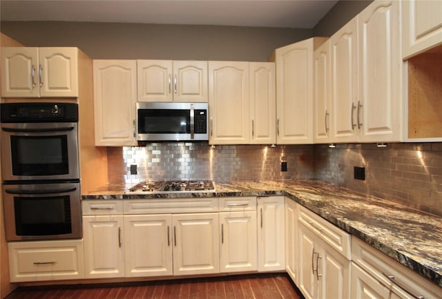 kitchen with backsplash, stainless steel appliances, dark hardwood / wood-style flooring, and dark stone countertops