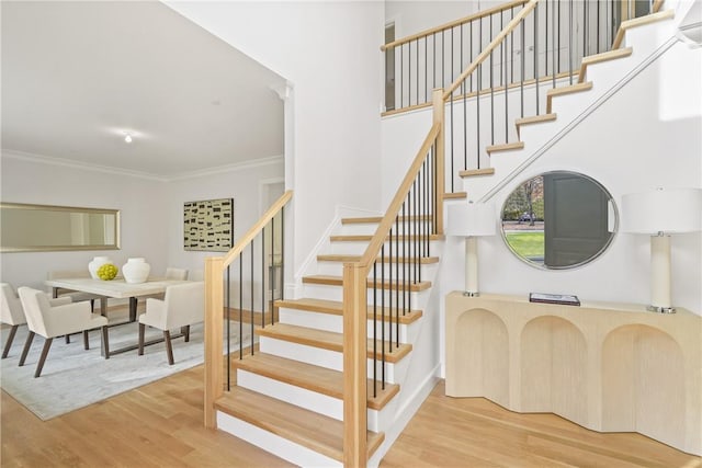 stairs with hardwood / wood-style flooring, a towering ceiling, and crown molding