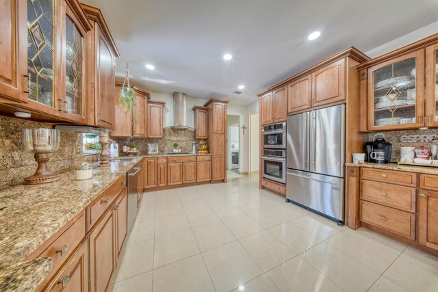 kitchen featuring tasteful backsplash, wall chimney range hood, light tile patterned floors, and appliances with stainless steel finishes