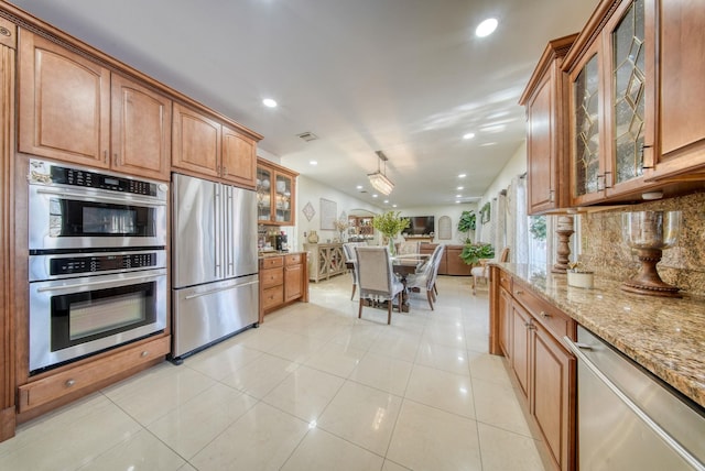 kitchen with light stone countertops, appliances with stainless steel finishes, light tile patterned floors, and backsplash