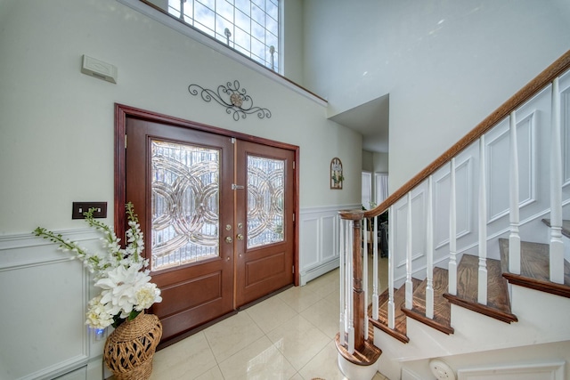 foyer entrance featuring a baseboard radiator, a towering ceiling, light tile patterned floors, and french doors