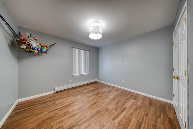 spare room featuring baseboard heating and light hardwood / wood-style flooring