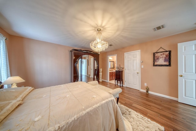 bedroom featuring an inviting chandelier, connected bathroom, and hardwood / wood-style flooring