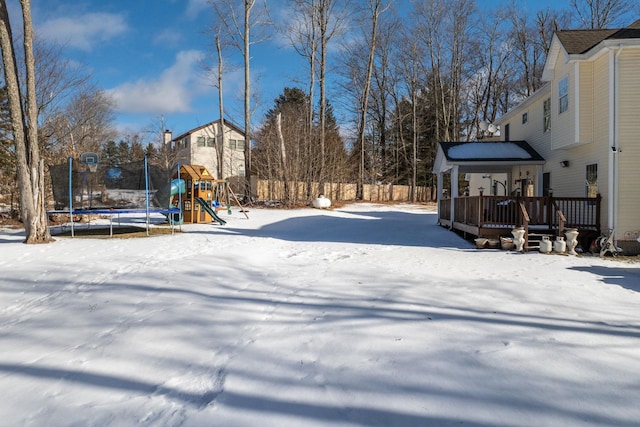 snowy yard featuring a playground, a deck, and a trampoline