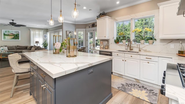 kitchen with sink, white cabinetry, light stone counters, hanging light fixtures, and a kitchen island