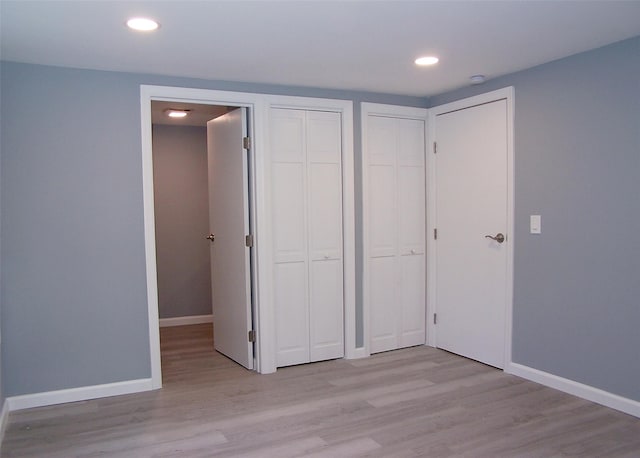 unfurnished bedroom featuring multiple closets and light hardwood / wood-style floors